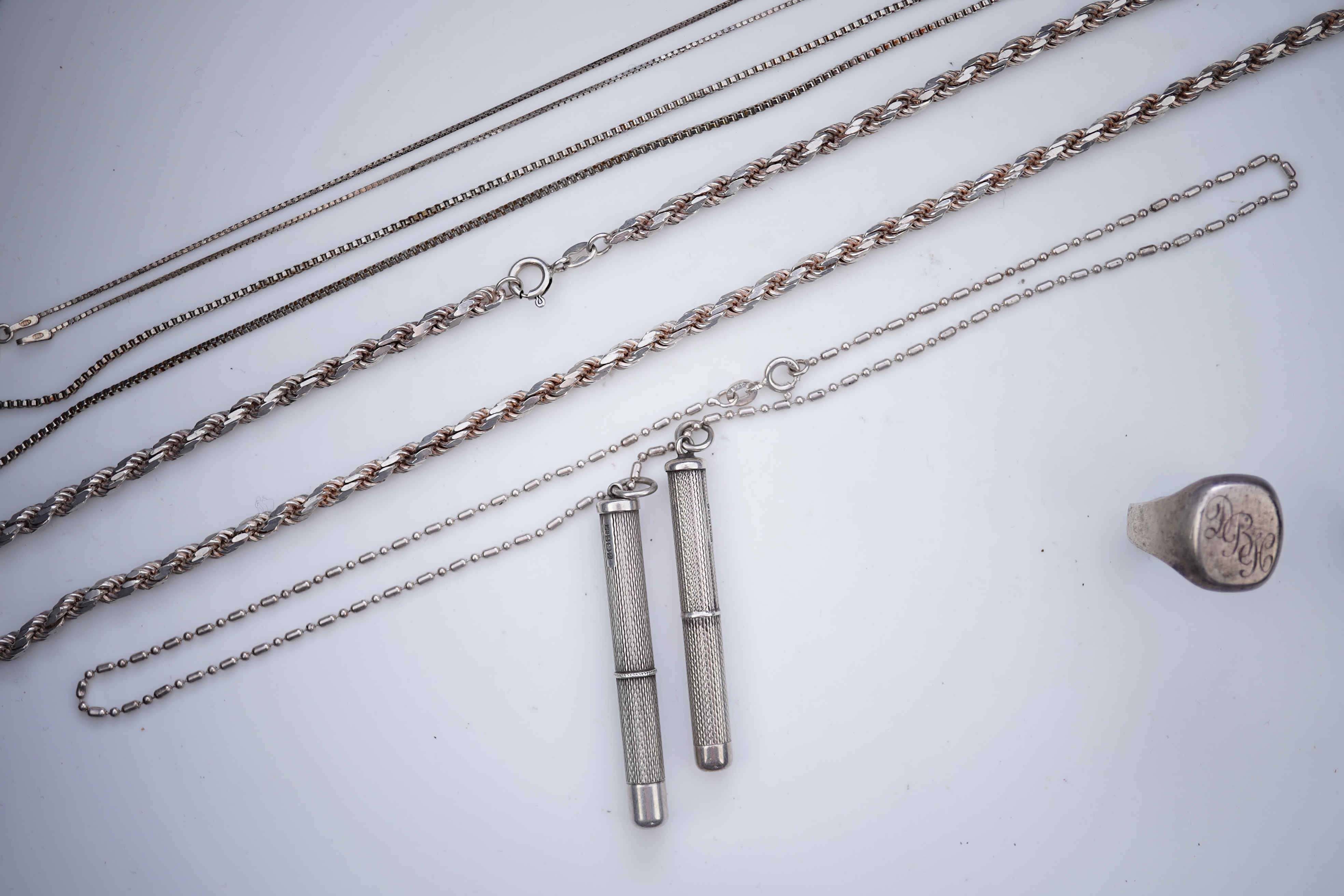 A collection of silver jewels, comprising: a bangle; a chain necklace suspending two winding toothpicks, one with toothpick deficient; a rope twist chain; a pair of cufflinks with the initials DBH; a pendant of abstract